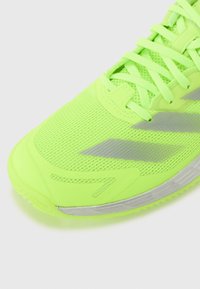 Neon zelená športová obuv s sieťovaným vrchom, textúrovanou podrážkou, reflexnými akcentmi a plochými šnúrkami, navrhnutá pre pohodlie a výkon.