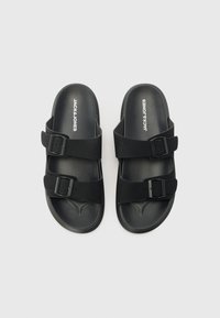 Sorte sandaler i svart med to justerbare spenner, laget av teksturert syntetisk materiale. Har en formet fotbed for komfort.