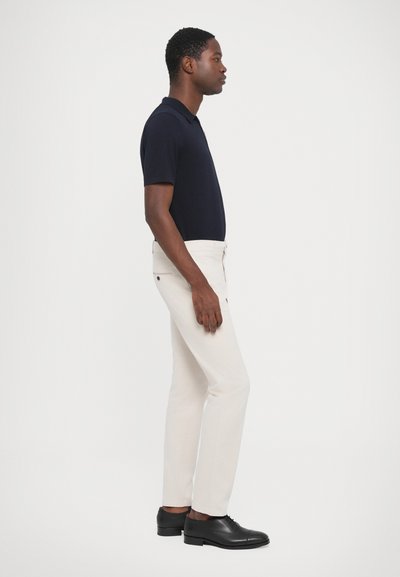 Cămașă polo bleumarin, pantaloni bej cu croială ajustată și pantofi negri. Pantalonii au buzunare laterale și un design slim fit. Linii curate, textură netedă.
