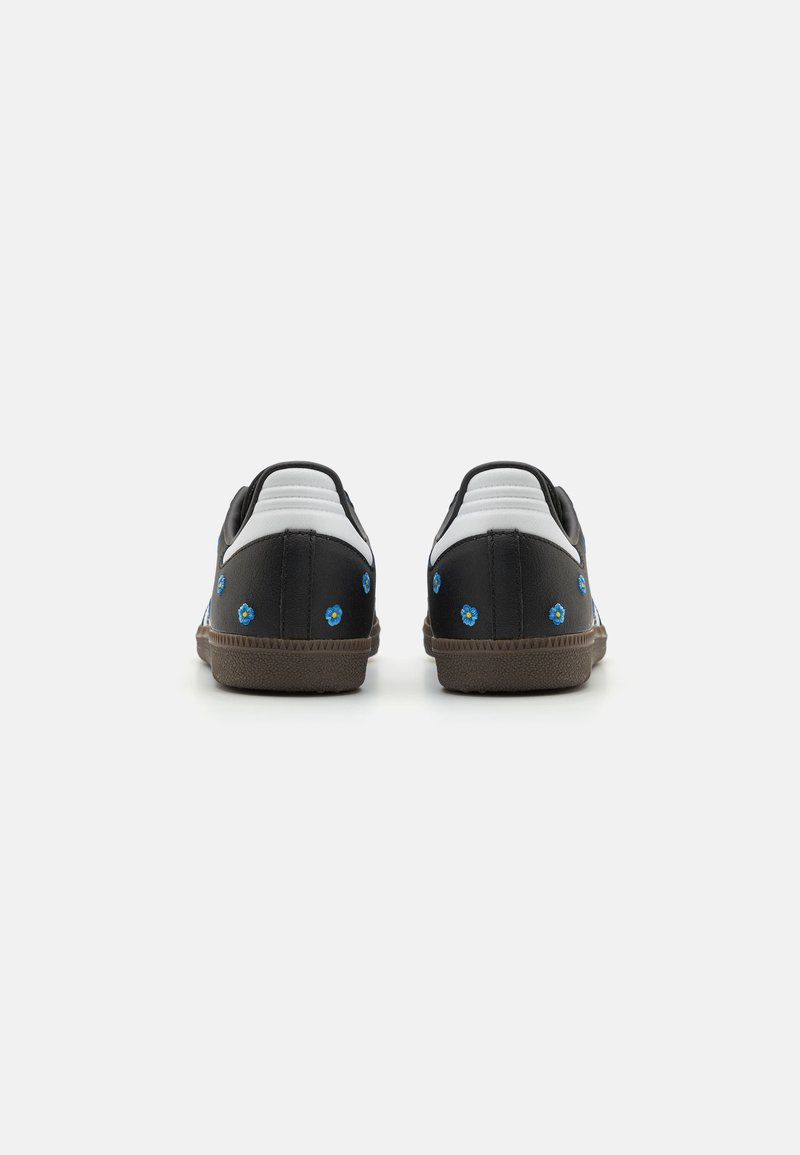 Zapatillas en blanco y negro con flores bordadas en azul, panel trasero texturizado, suela de goma marrón y parte superior de cuero suave.