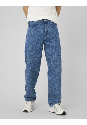 Jean bleu avec un léger motif cachemire, porté avec des baskets blanches et une chemise blanche rentrée.