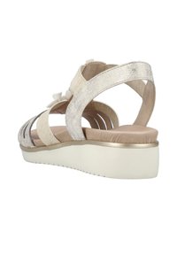 Öppen tå sandal i metallisk silver och beige, med utskärningsdesign, justerbara remmar och en vadderad beige sula med ett guldfynd.