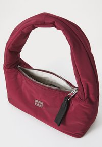 Geantă din nylon bordo cu un mâner rotund, căptușit, fermoar argintiu și un interior alb în contrast. Prezintă o plăcuță cu logo pe față.