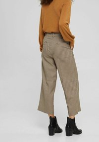 Rutmönstrade högmidjade byxor i beige och brunt, med en vid benmodell. Kombinationen med svarta ankelboots och en brun tröja.