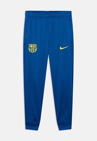 Μπλε αθλητικό παντελόνι από λείο ύφασμα, με κίτρινο λογότυπο Nike στο μπροστινό μέρος και έμβλημα της FC Barcelona στο πλάι.
