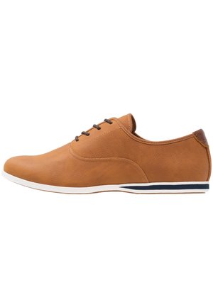 Brun afslappet snøresko med hvid sål og mørkeblå stribe, med glat lædertekstur og minimale syningsdetaljer.