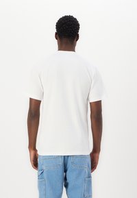 White cotton t-shirt with a crew neck and short sleeves, viewed from the back, paired with light blue cargo pants.