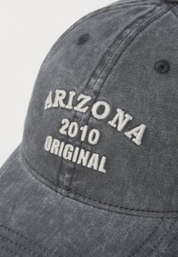 Grijze pet van katoen met gebogen rand. Bevat witte geborduurde tekst: "ARIZONA 2010 ORIGINAL." De tekst heeft een iets verhoogde structuur.