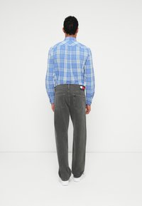 Ανδρικό μπλε �καρό πουκάμισο με κουμπιά, συνδυασμένο με γκρι τζιν ευθείας γραμμής. Σημαντικές λεπτομέρειες περιλαμβάνουν μια ετικέτα με λογότυπο στα τζιν και μια λεία υφή υφάσματος.