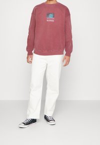 Mörkröd fleece sweatshirt med rund hals och grafiskt tryck, kombinerad med vita vida byxor och svarta kanvas sneakers.