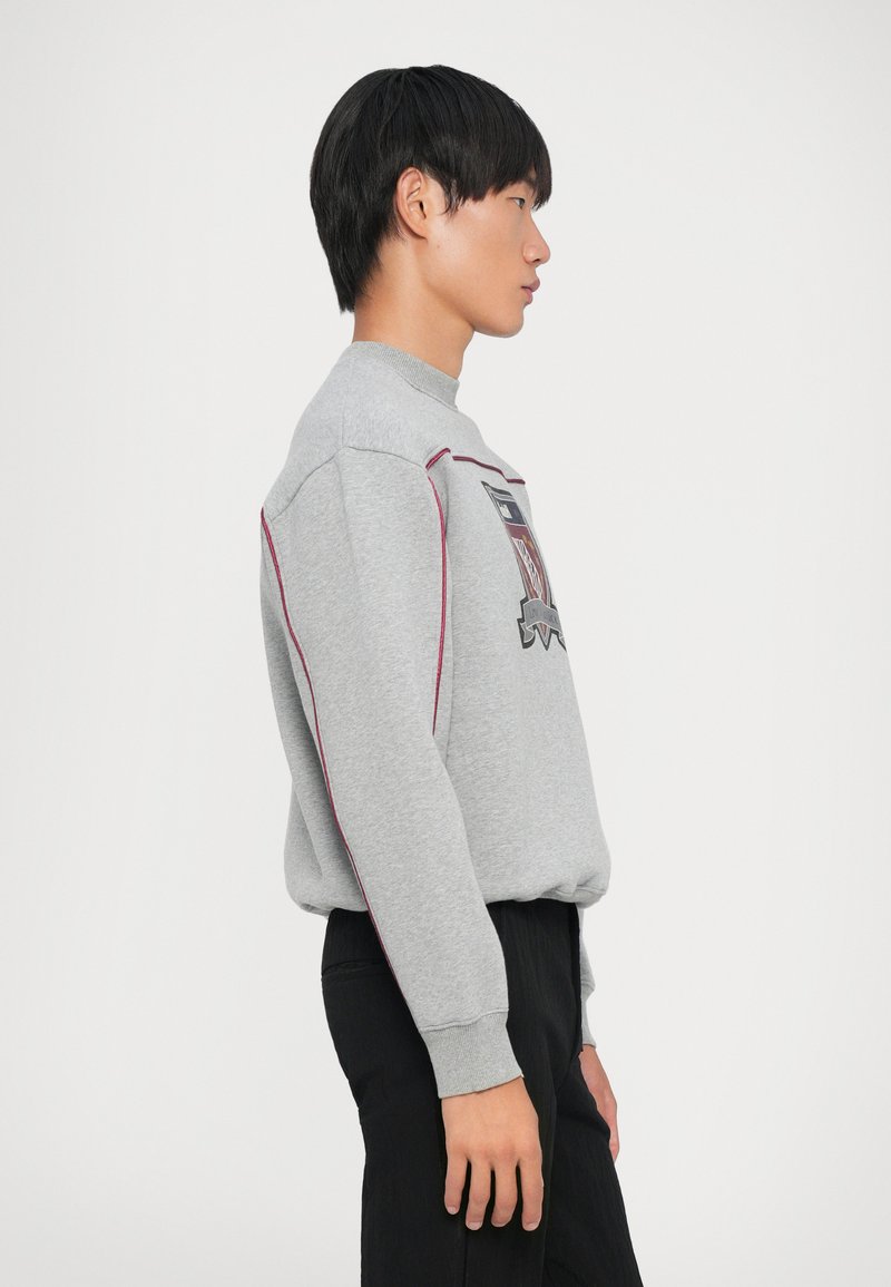 Grå sweatshirt med rund halsudskæring, ribbede manchetter og lyserød stikning. Har et grafisk print foran.