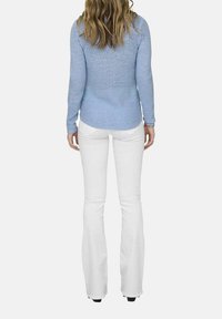 Maglione azzurro chiaro in maglia con maniche lunghe, design aderente, abbinato a pantaloni bianchi a campana, visto da dietro. La texture è liscia.