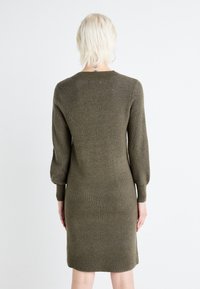 Abito a maglia verde oliva con maniche lunghe, leggermente puffate e scollo rotondo. Tessuto a coste in tutta la sua lunghezza, silhouette aderente.