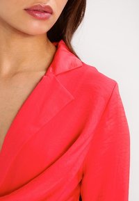 Robe portefeuille rose vif avec un col et un tissu doux et léger. Un design drapé met en valeur les épaules et le décolleté.