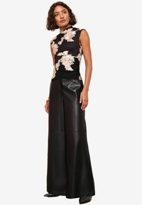 Sort ærmeløs top med blomsterbroderi i beige, parret med brede ben i sort læder. Outfittet har en tætsiddende silhuet.
