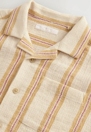 Beige shirt met een textuurweefsel, voorzien van gele en rode gestreepte accenten. Inclusief een kraag en een borstzak met knoopsluiting.