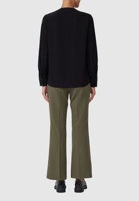 Schwarze Bluse mit langen Ärmeln und knöpfbaren Manschetten, kombiniert mit olivgrünen, weit geschnittenen Hosen, die eine glatte Textur und eine lockere Passform aufweisen.