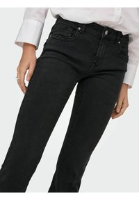 Vaqueros de denim negro con un corte ajustado, que cuentan con cinco bolsillos, un cierre de botón y cremallera, y una textura suave.
