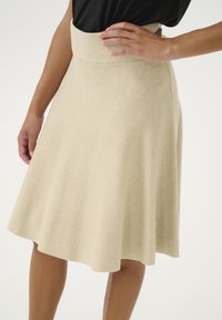 Beige színű, enyhén flared szoknya sima textúrával, magas derékkal és térd alatti hem-el. Az anyag könnyűnek és kissé rugalmasnak tűnik.