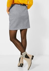 Grå ullkjol med fickor, dragkedja bak, kombinerad med beige ankelstövlar med svarta accenter och ribbade grå strumpor. Genomskinliga svarta strumpbyxor.