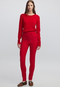 Maglione rosso a maniche lunghe abbinato a pantaloni rossi aderenti. Il maglione ha una texture morbida; i pantaloni presentano una finitura liscia e cuciture sottili. Ballerine con stampa animalier.