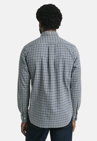Camisa de manga larga a cuadros en azul marino y blanco. Cuenta con un cuello abotonado y un pliegue en la parte posterior. Tela de algodón con una textura suave.