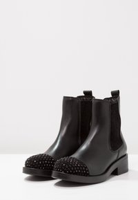 Bottines noires en cuir lisse avec des côtés en tissu texturé et un capuchon de bout clouté. Petit talon carré et tirettes à l'arrière.