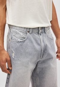 Ανοιχτό μπλε τζιν παντελόνι με χαλαρή εφαρμογή, που διαθέτει φθαρμένο σχέδιο στο μηρό και παραδοσιακή πεντα-pocket σχεδίαση.