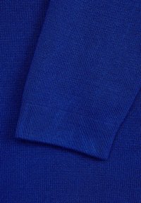 Blå stickad tröja med ribbad textur och slät yta. Materialet ser mjukt ut, med en jämn vävning genom hela tyget.