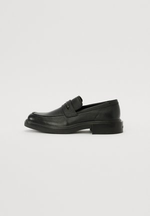 Mocassins en cuir noir avec un bout arrondi, design à enfiler et finition texturée. Comprend un petit talon carré et des accents de quincaillerie minimalistes.