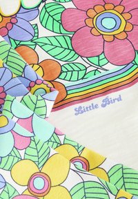 Barevná látka s květinovými vzory v růžové, fialové, žluté a zelené barvě. Lehká textura, s nápisem "Little Bird" napsaným kurzívou.