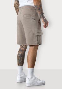 Shorts cargo beige avec une taille élastique, poches latérales et détail de logo brodé. Associés à des baskets blanches et des chaussettes côtelées.