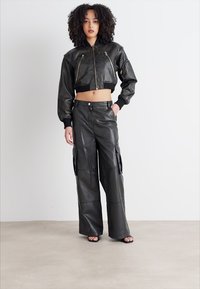 Černá kožená zkrácená bomber bunda s kapsami na zip, spárovaná s odpovídajícími volnými cargo kalhotami s bočními kapsami a zapínáním na knoflík.