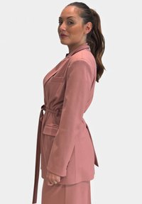Blazer rosa chiaro su misura con cintura, tasca frontale singola e maniche lunghe, abbinato a un tessuto liscio e design strutturato.