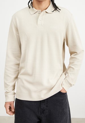 Beige longsleeve poloshirt van ribstof, met een kraag, een knoopjespat en een subtiele logodetail op de borst.