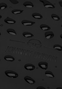 Black textured surface with raindrop-shaped cutouts, featuring the embossed text "JOHNNY URBAN" and a circular logo above it.