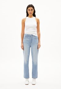 Top in cotone bianco a costine abbinato a jeans in denim blu chiaro a gamba dritta. Sneakers bianche completano l'outfit. Design semplice, linee pulite.