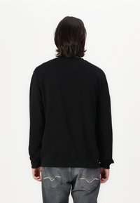 Sudadera negra de manga larga, cuello redondo y puños acanalados. Combinada con jeans grises que presentan costuras decorativas en los bolsillos traseros.