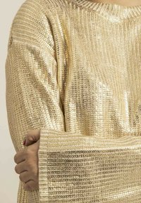 Pull en métal doré avec un design texturé en côtes et des manches larges. Présente une coupe ample et une surface douce et scintillante.