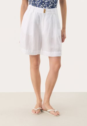 Pantaloni corti in lino bianco con vita alta, dotati di chiusura a doppio bottone e risvolti, abbinati a ciabatte leggere.