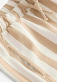 Tissu rayé beige et blanc avec une taille à cordon de serrage et des poches cousues. Le matériau semble doux avec une texture lisse.