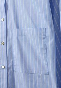 Light blue striped button-up shirt featuring thin white vertical stripes, a chest pocket, and a smooth texture with a classic collar.