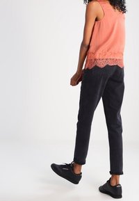 Jasnoróżowa bezrękawnik z koronkowym wykończeniem, zestawiony z czarnymi zwężanymi spodniami i czarnymi trampkami. Gładki materiał, luźny krój i podwinięte mankiety.