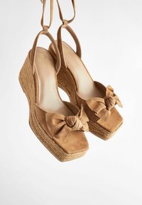 Sandales à talons compensés en suede marron avec un bout carré, un détail en noeud sur la tige, et une base en jute texturé; dotées de brides arrière.