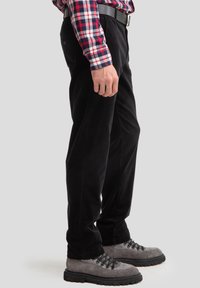 Pantalons en velours côtelé noir avec une coupe droite, dotés de poches latérales, portés avec une chemise à carreaux et des bottes en daim grises.