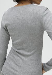 Woman wearing a fitted long-sleeve gray shirt shown from the back with a small tattoo on the upper neck.
