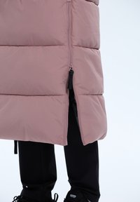 Eenvoudig roze gewatteerd vest met een rits aan de voorkant, voorzien van een hoge kraag en een zijsplit, gecombineerd met zwarte broeken en schoenen. Soepele textuur.