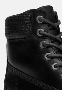 Černé kožené kotníkové boty s texturovaným tkaným svrškem, šedými očky a odpovídajícími tkaničkami. Obsahují decentní logotyp na boku.