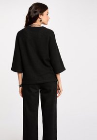 Maglione nero a maglia con maniche a tre quarti, scollatura rotonda e vestibilità comoda. Indossato con pantaloni a palazzo neri a vita alta.
