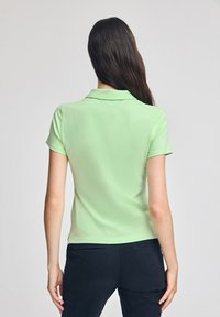 Ljusgrön pikétröja med kort ärm och krage. Tillverkad av mjukt tyg, har en figursydd design och passar bra ihop med mörka byxor.